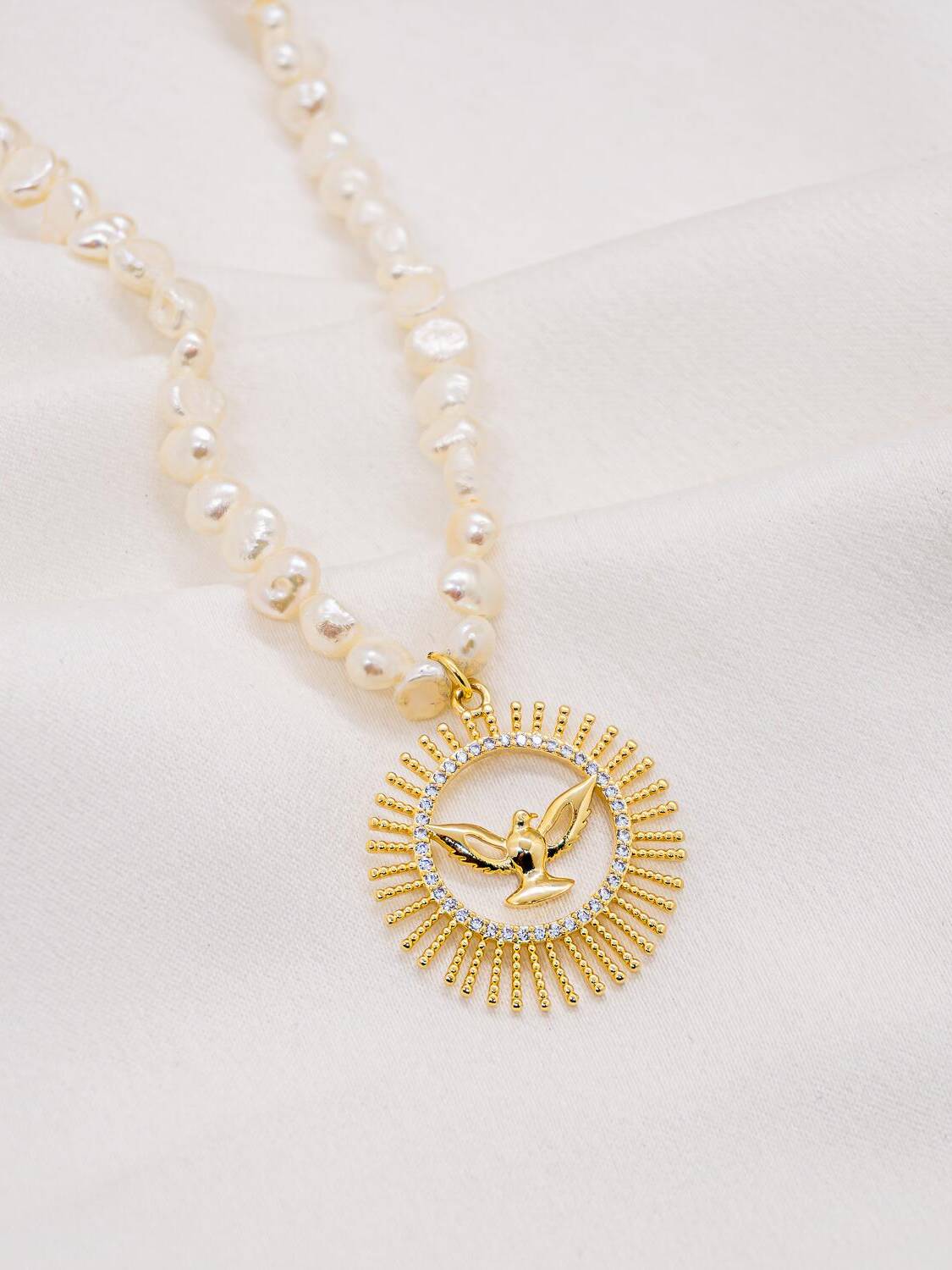 Collier de perles blanches irrégulières, médaille ronde dorée à colombe en relief, cercle de pierres claires