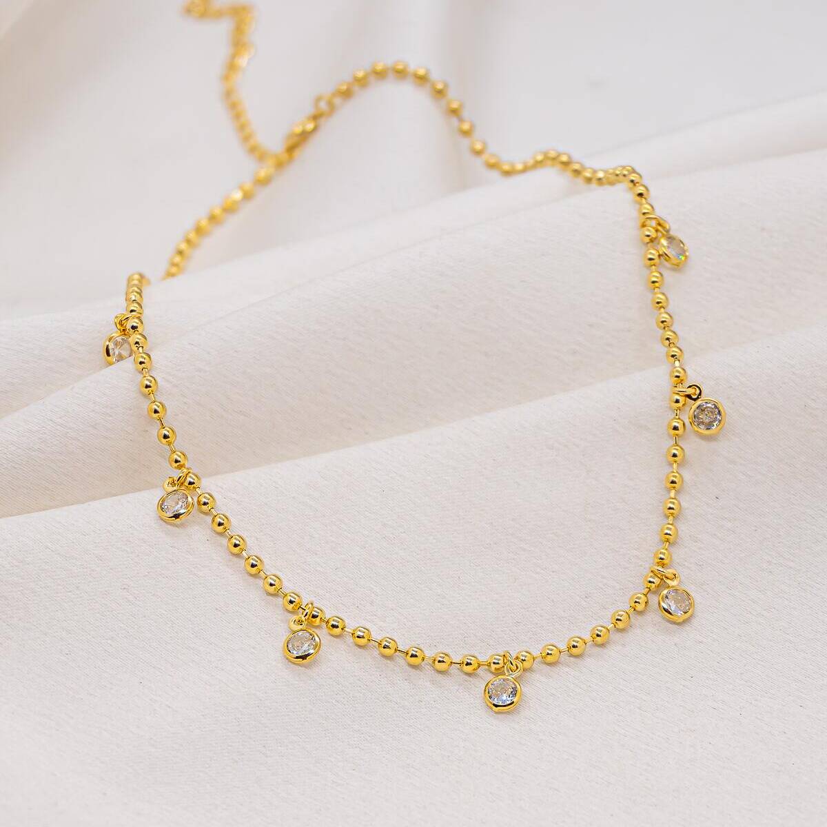 Gold beaded choker with dangling pavé-set clear stones, on white fabric
