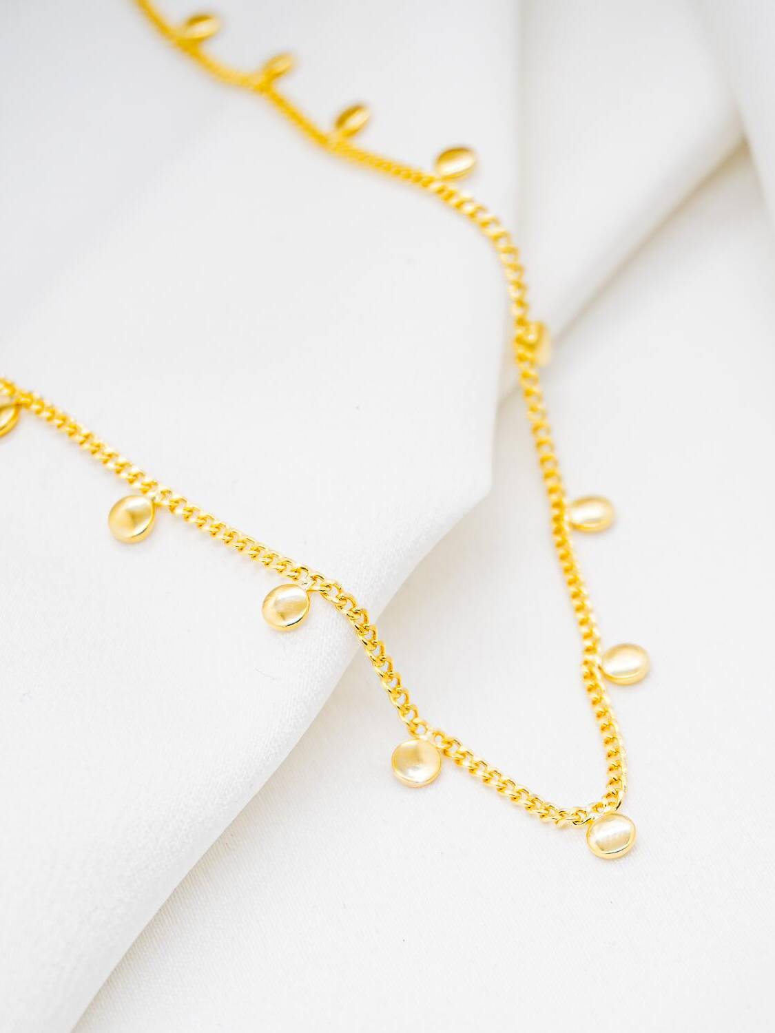 Collier ras-de-cou doré à chaîne serrée et petites plaques rondes lisses pendantes, sur tissu blanc