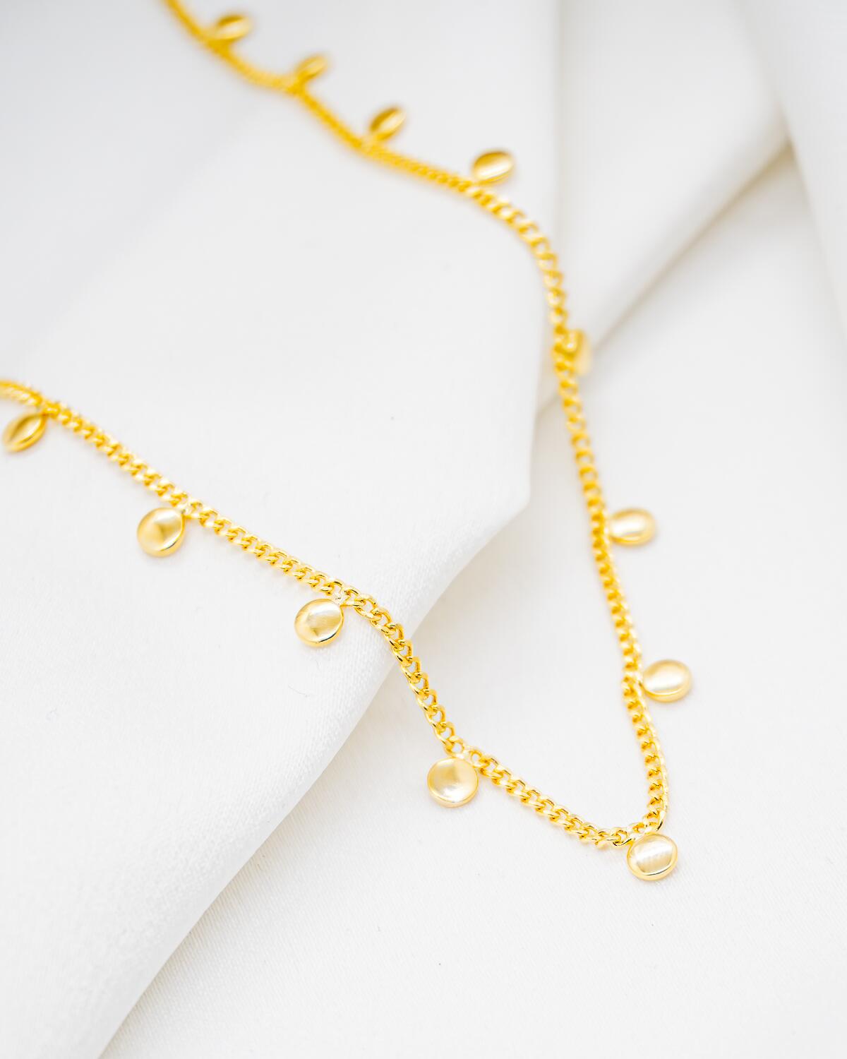 Collier ras-de-cou doré à chaîne serrée et petites plaques rondes lisses pendantes, sur tissu blanc