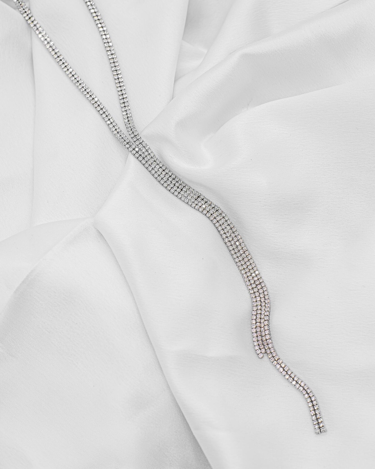 Long collier rivière argenté en rangées de pierres claires serrées, extrémités retombant en cascade