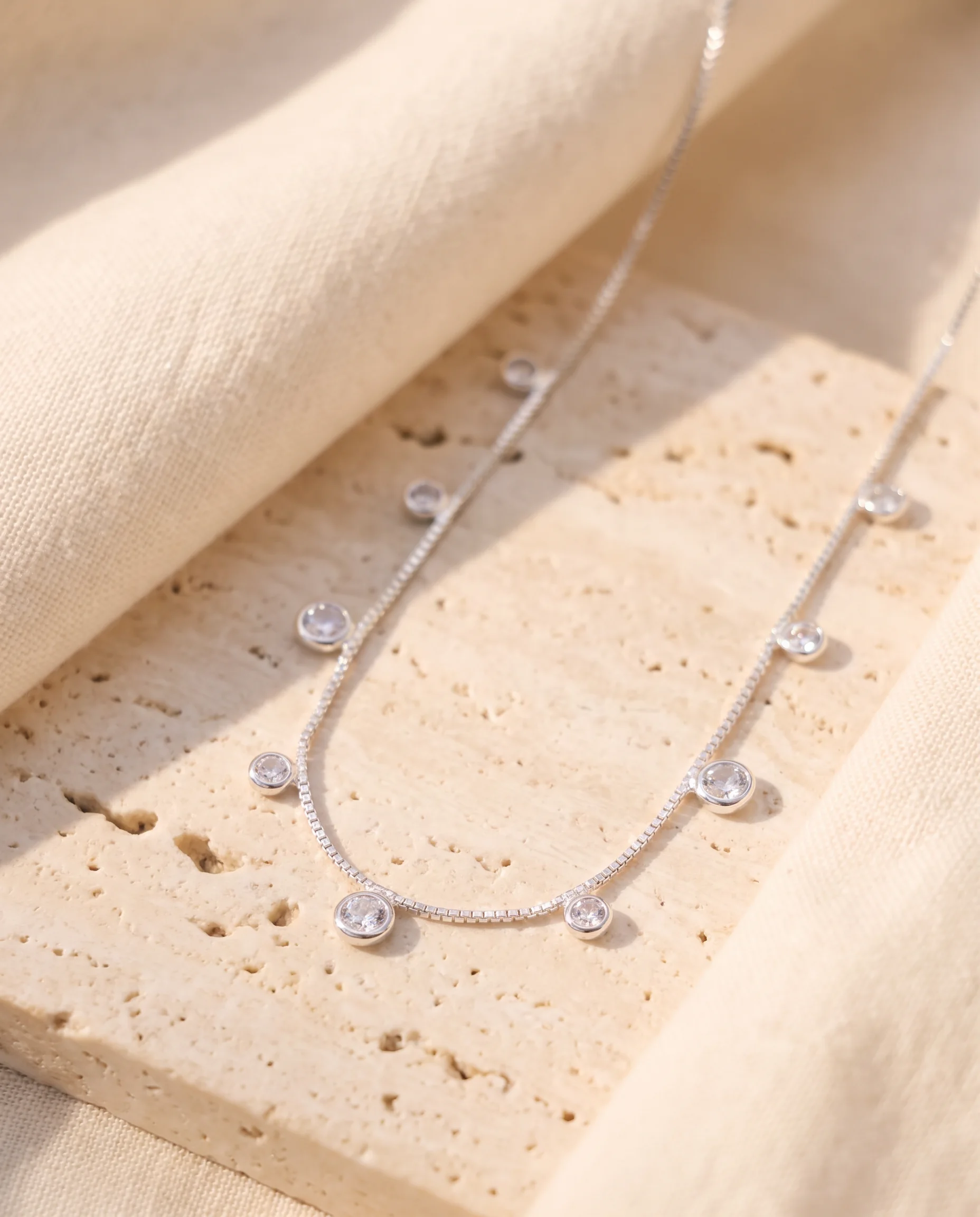 Silver Venetian chain necklace with bezel-set sparkling stones, displayed on a clear stone