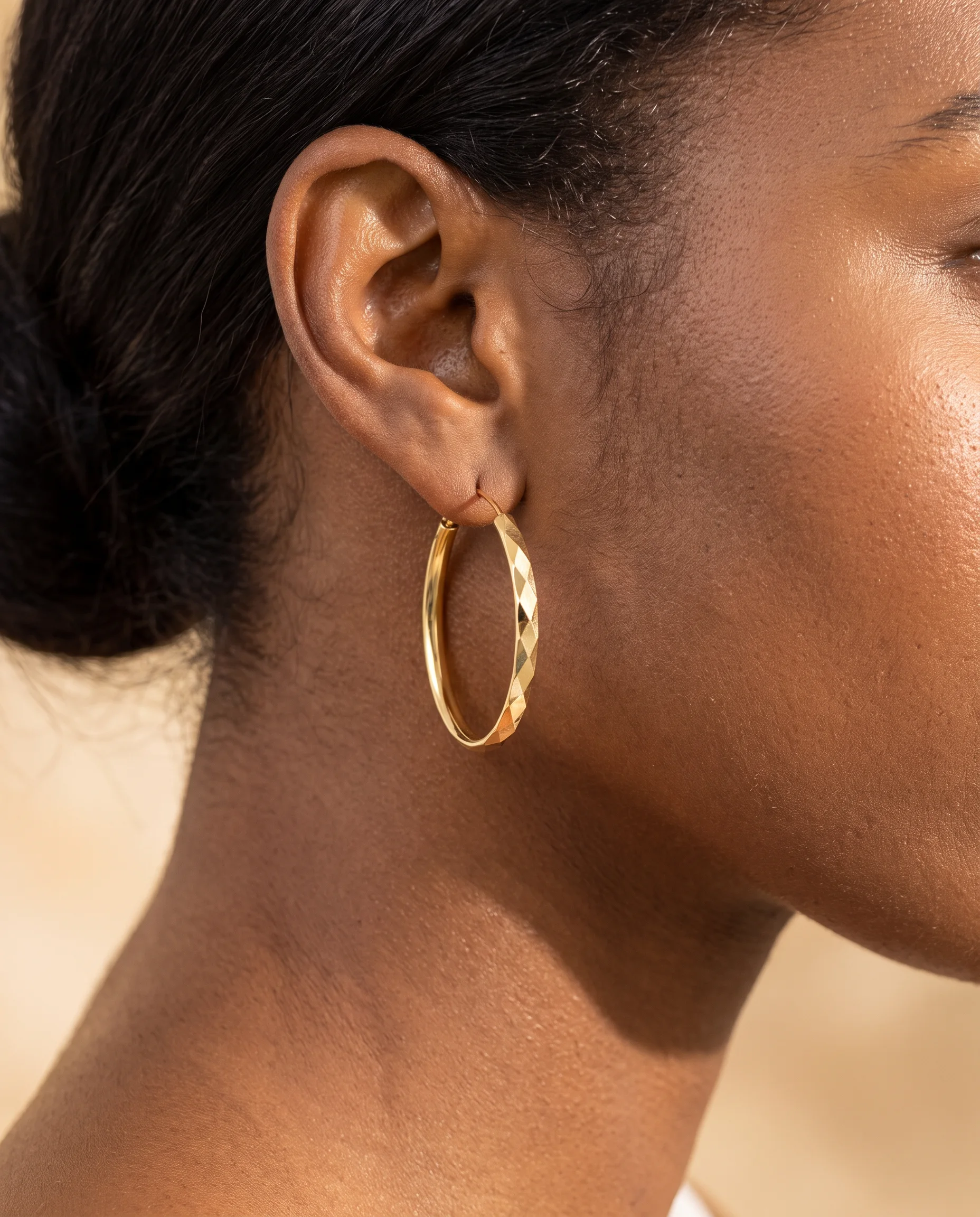 Gold faceted hoop earring worn on the ear, side view