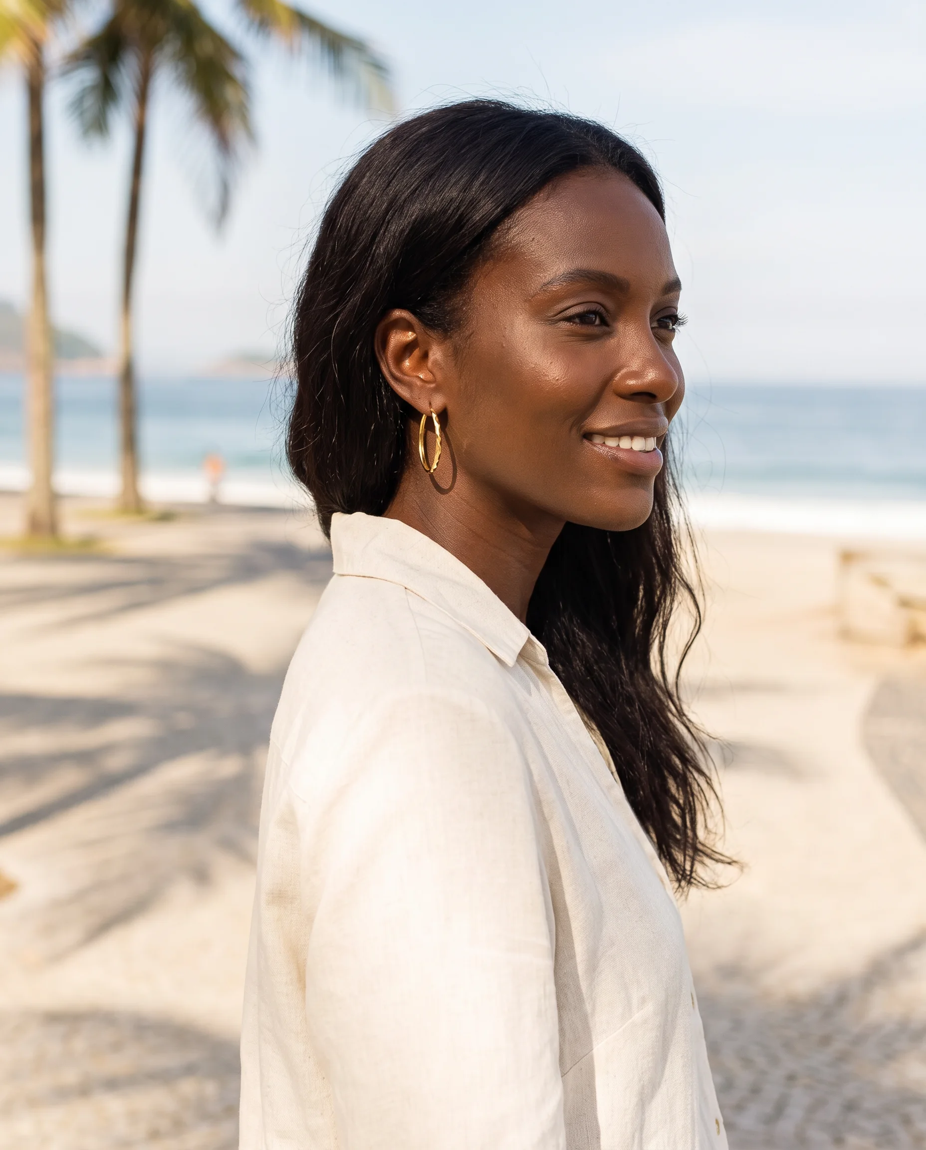 Woman in a linen shirt wearing gold hoop earrings on a seaside walk