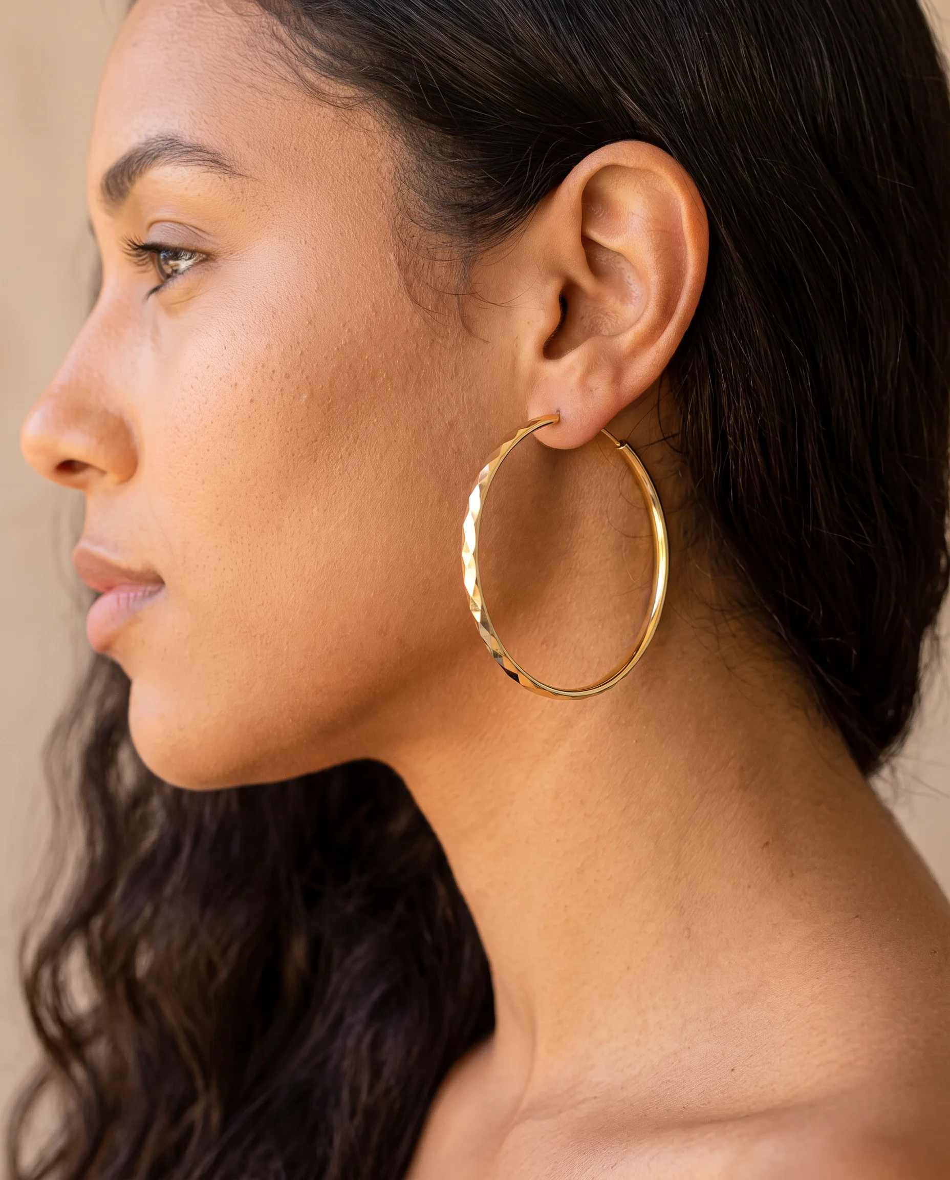 Large gold faceted hoop worn on ear, profile view