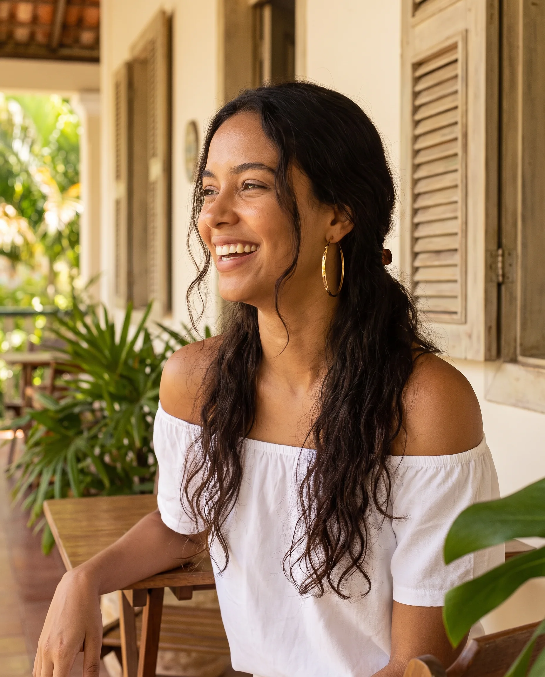 Smiling woman under a veranda, large gold hoops on her ears