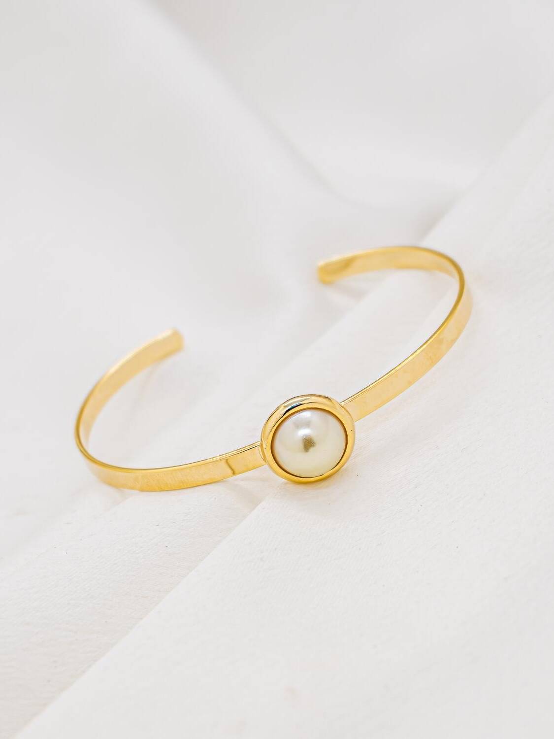 Jonc ouvert doré plat avec demi-perle ronde crème au centre, sur tissu blanc