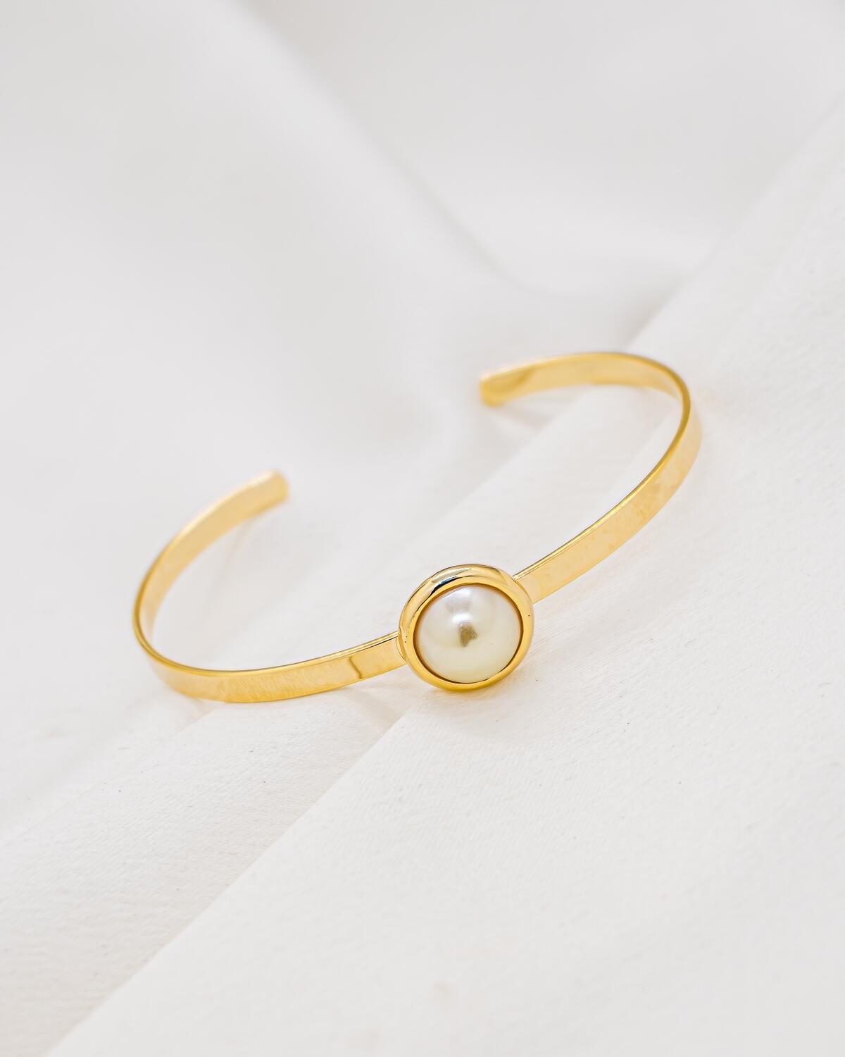 Jonc ouvert doré plat avec demi-perle ronde crème au centre, sur tissu blanc