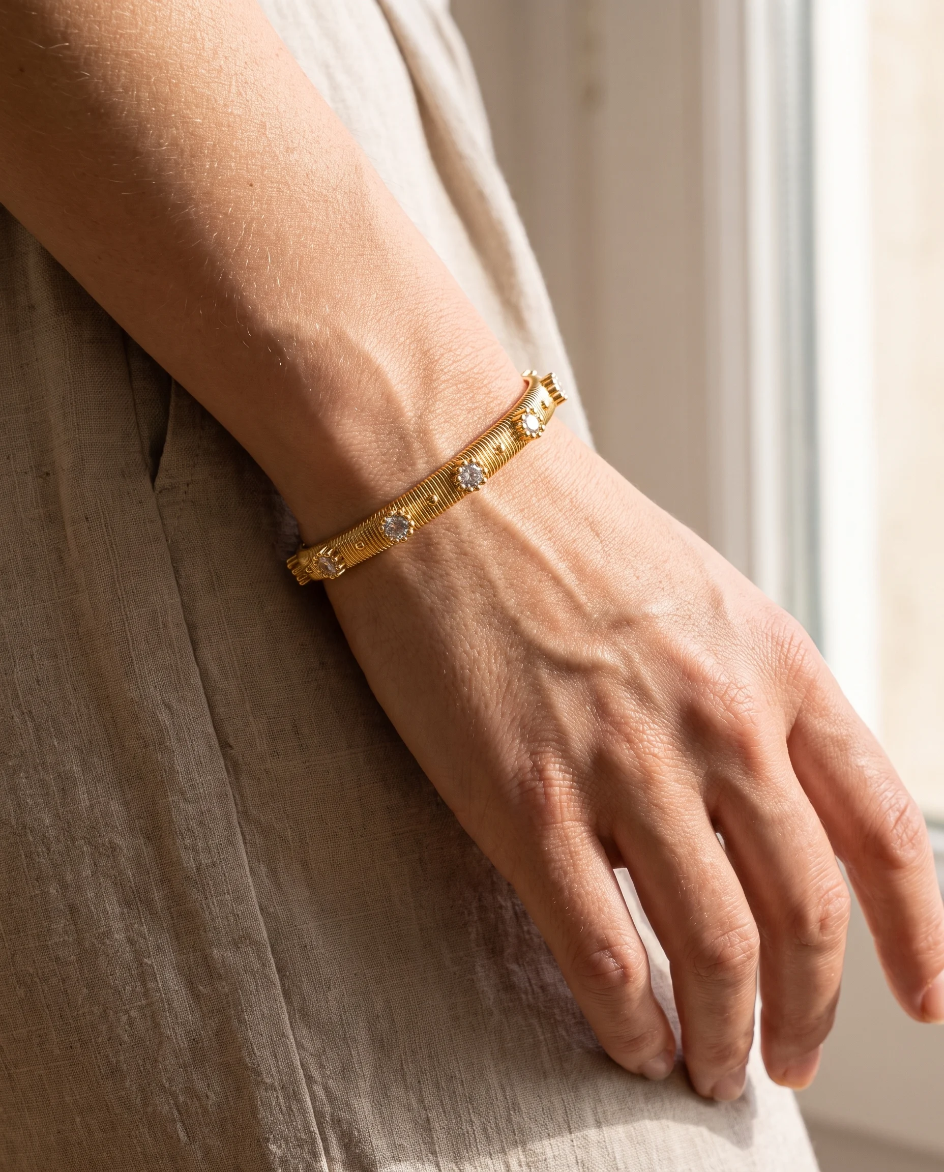 Bracelete rígido com pequenas estrias e pontos de luz, usado no pulso, visto de perto