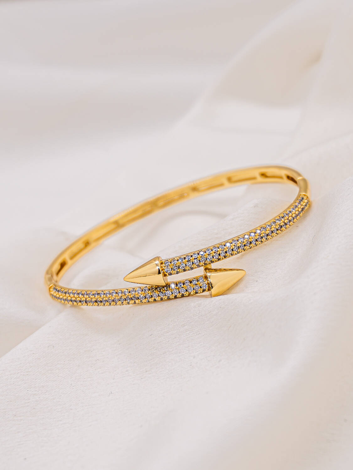 Jonc doré ouvert aux pointes de flèche, pavé de petites pierres claires, sur tissu blanc