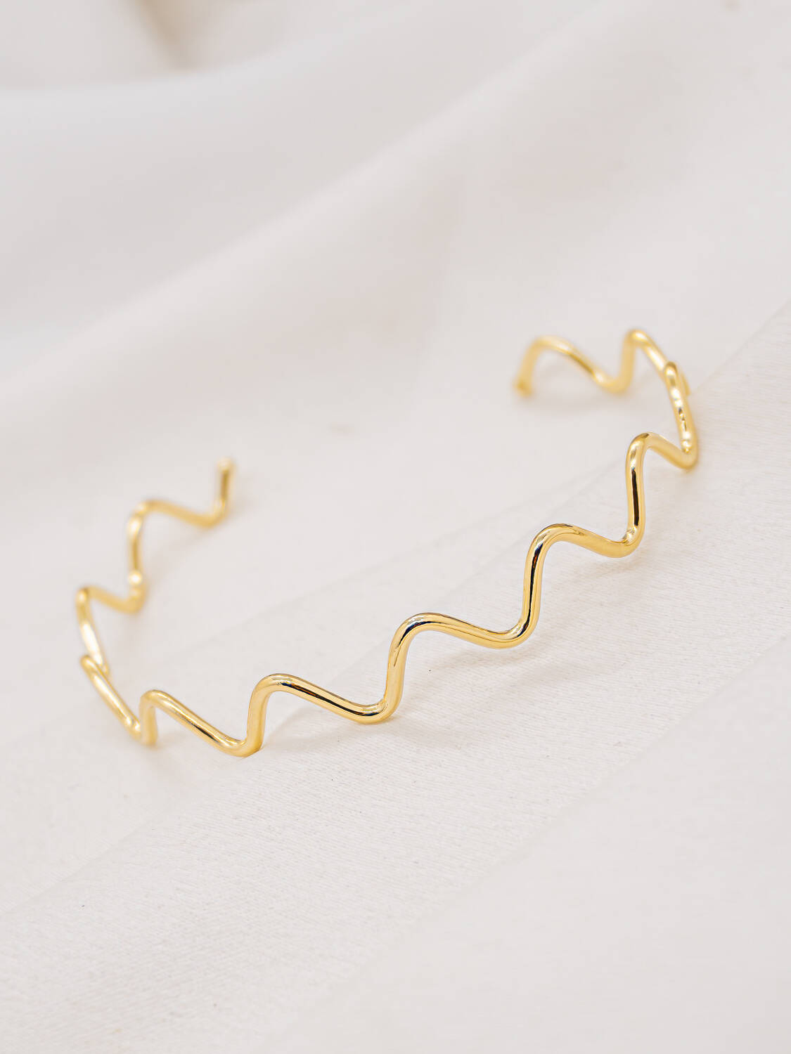 Jonc ouvert en fil d’or lisse formant un zigzag régulier, sur un tissu blanc cassé