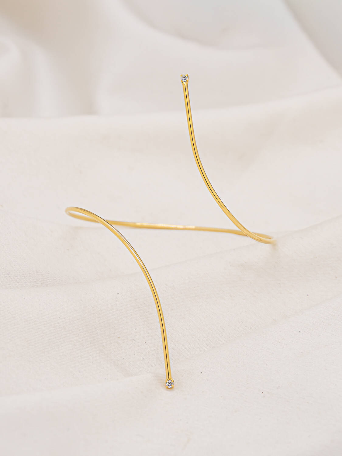 Jonc ouvert en fil doré formant une spirale, chaque extrémité ornée d’une minuscule pierre claire